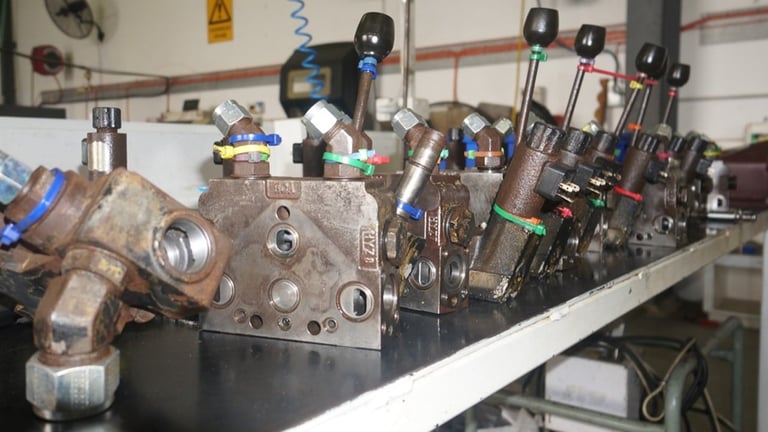 Cluttered workbench with machine parts, cylinders, and various mechanical components and tools arranged on a white table