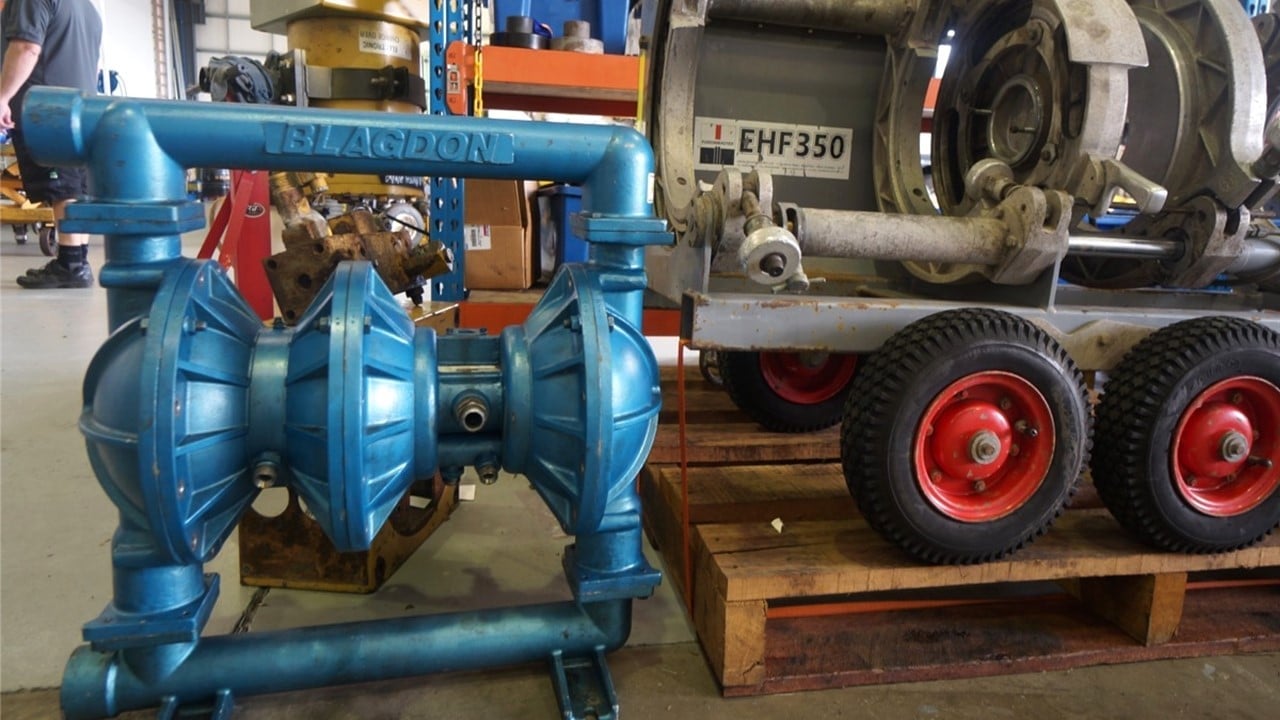 Blue double-diaphragm pump on wooden base in industrial workshop with motor and trailer equipment